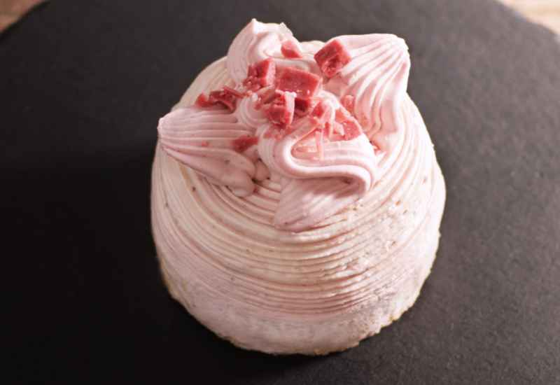 ピンク色の花のようにきれいなしぼりのクリームにフランボワーズクランチチョコを散りばめた丸形のかわいいレアチーズケーキ